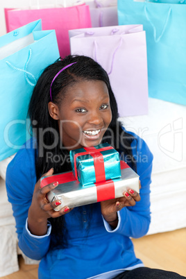 Cheerful woman holding a present sitting on the floor
