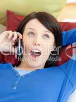 Surprised young woman talking on phone lying on a sofa
