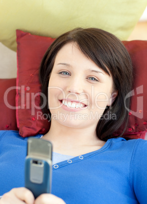 Smiling teen girl sending a text lying on a sofa