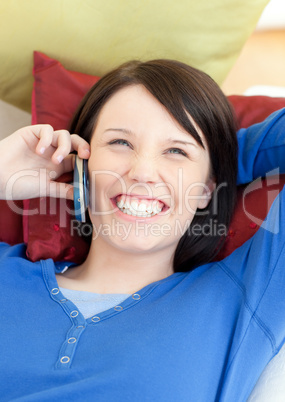 Laughing young woman talking on phone lying on a sofa