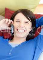 Laughing young woman talking on phone lying on a sofa