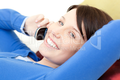 Joyful young woman talking on phone lying on a sofa