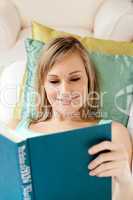 Smiling woman reading a book lying on a sofa