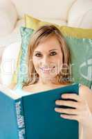 Charming woman reading a book lying on a sofa