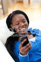Happy woman sending a text lying on a sofa