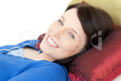Cheerful young woman listening music lying on a sofa