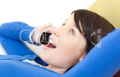 Astonished young woman talking on phone lying on a sofa