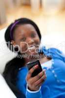 Afro-American woman sending a text lying on a sofa