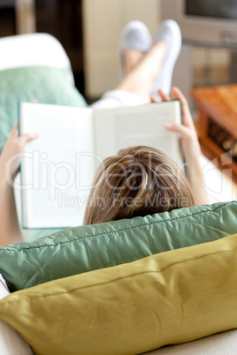 Blond woman reading a book lying on a sofa