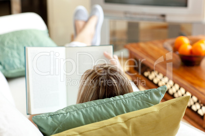 Caucasian woman reading a book lying on a sofa