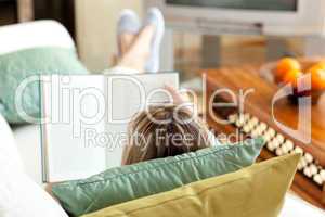 Caucasian woman reading a book lying on a sofa