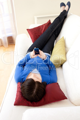 Brunette teen girl sending a text lying on a sofa