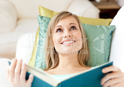 Jolly woman reading a book lying on a sofa