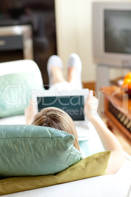 Blond woman using a laptop lying on a sofa