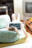 Blond woman using a laptop lying on a sofa