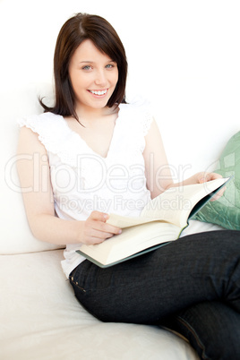 Cheerful woman reading a book sitting on a sofa