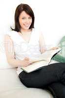 Cheerful woman reading a book sitting on a sofa