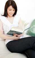 Concentrated woman reading a book sitting on a sofa