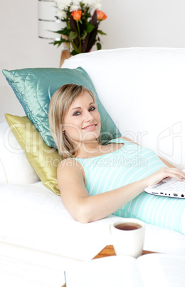 Radiant woman using a laptop lying on a sofa