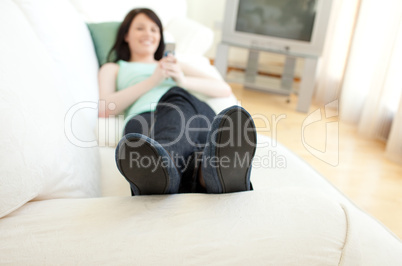 Brunette woman sending a text lying on a sofa