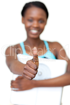 Cheerful fitness woman with thumb up holding a weight scale