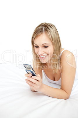 Smiling woman sending a text lying on her bed