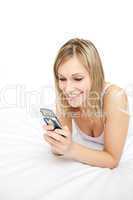 Smiling woman sending a text lying on her bed