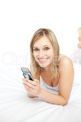 Jolly woman sending a text lying on her bed