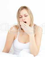 Exhausted woman yawning sitting on her bed