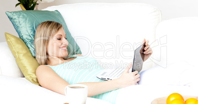 Happy woman using a laptop lying on a sofa