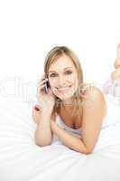 Happy woman talking on phone lying on her bed