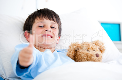 Little boy hugging a teddy bear lying in a hospital bed
