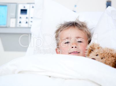 Sick adorable little boy lying in a hospital bed with his teddy