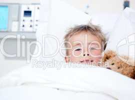 Sick adorable little boy lying in a hospital bed with his teddy