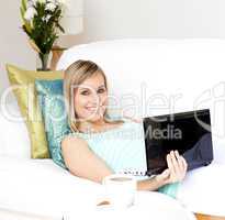 Delighted woman surfing the internet lying on a sofa