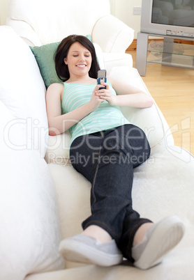 Cheerful woman sending a text lying on a sofa