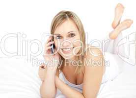 Delighted woman talking on phone lying on her bed