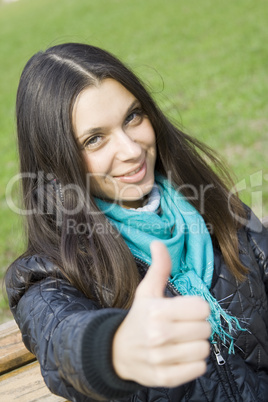 Beautiful girl in a park smiling. Thumb sign OK