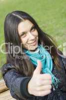 Beautiful girl in a park smiling. Thumb sign OK