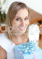 Cheerful young woman holding a present sitting on the floor