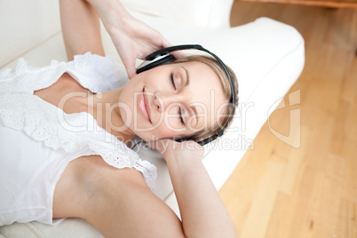 Cute young woman listening music lying on a sofa