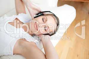 Cute young woman listening music lying on a sofa