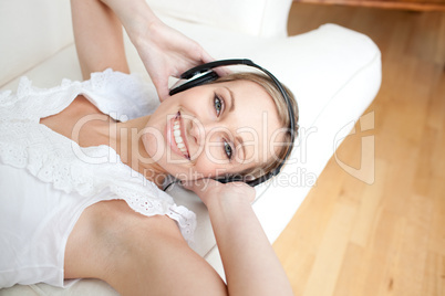 Smiling young woman listening music lying on a sofa