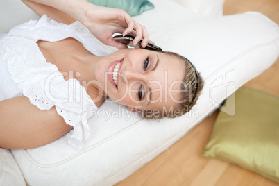 Happy woman talking on phone lying on a sofa