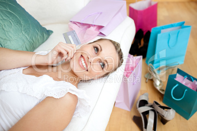 Bright woman holding a credit card surrounded with shopping bags