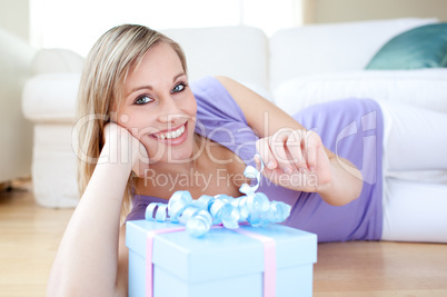 Delighted blond woman holding a present lying on the floor