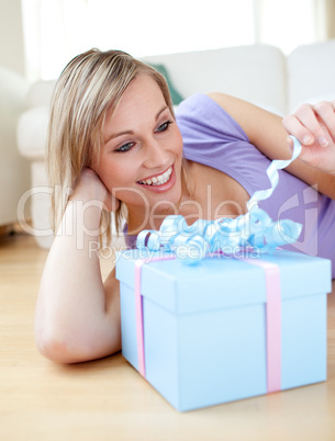 Cheerful blond woman holding a present lying on the floor