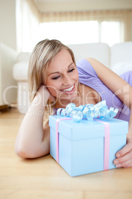 Happy blond woman holding a present lying on the floor