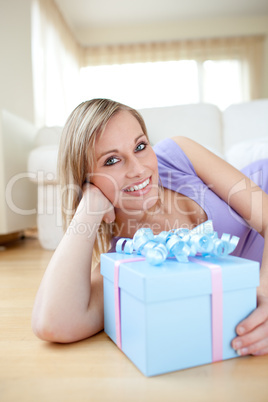 Bright woman holding a present lying on the floor