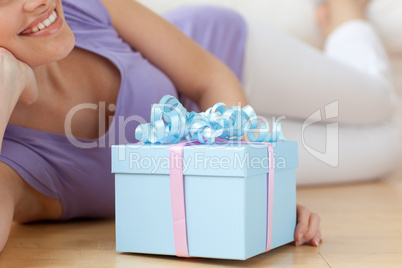 Smiling woman holding a present lying on the floor